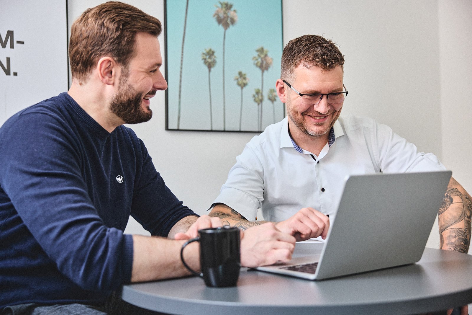 Zwei Kollegen lachen gemeinsam am Laptop